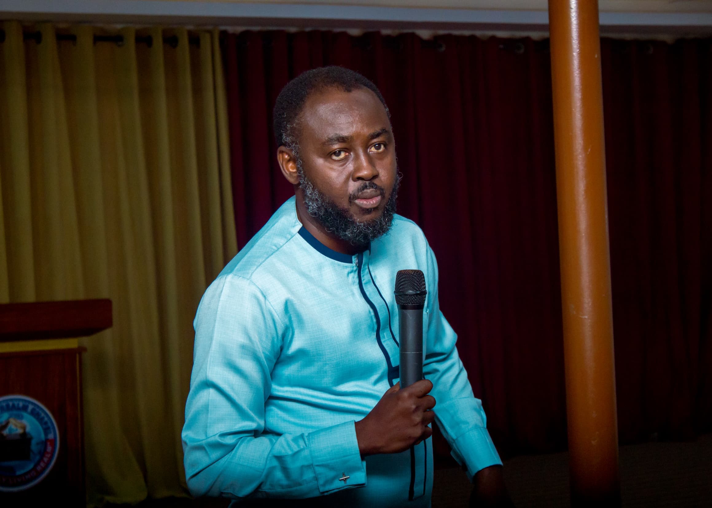 Apostle Benjamin Asamoah holding a microphone on stage